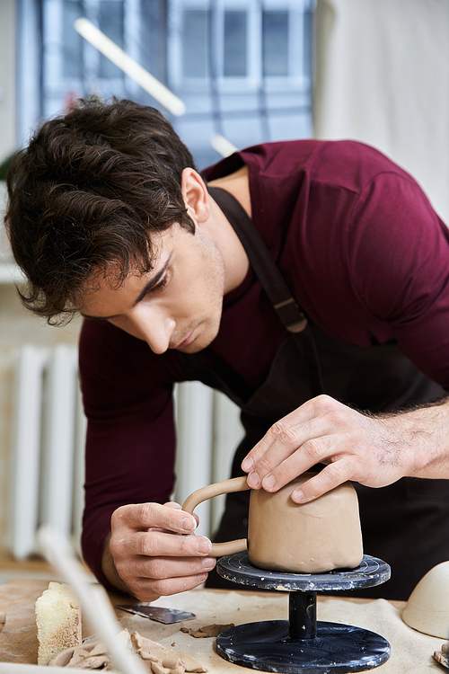 Alluring male in apron making some pottery in studio.