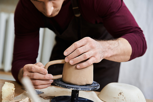 Young man in black apron making pottery with his hands.