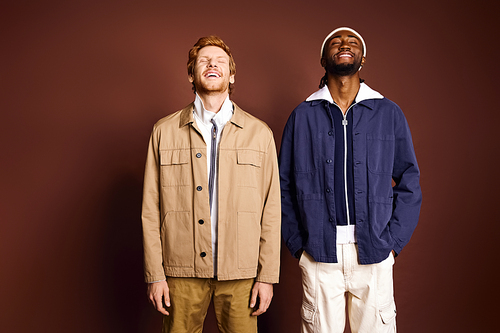 Two fashionable men stand by a brown wall.