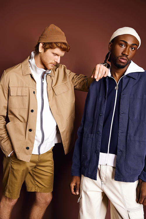 Multicultural men in fashionable attire standing next to each other in front of a brown wall.