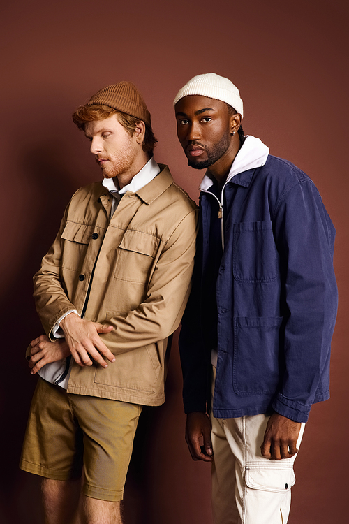 Two stylish men stand by a brown wall.