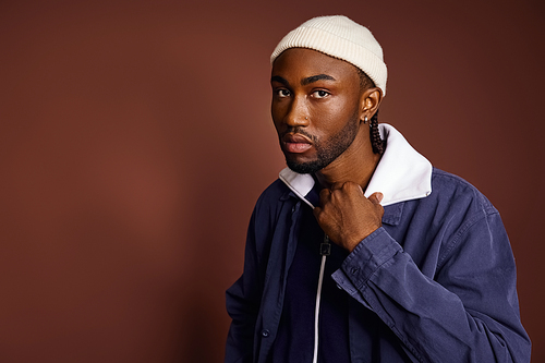 Young African American man in blue jacket and white hat.