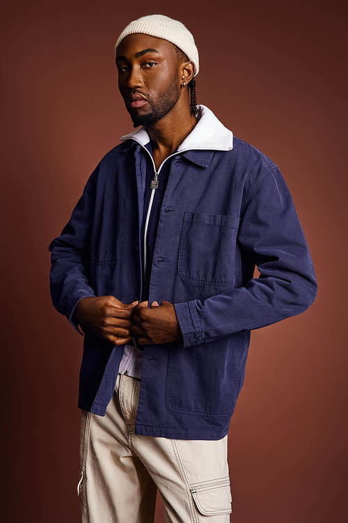 A handsome young African American man wearing a blue jacket and white hat.