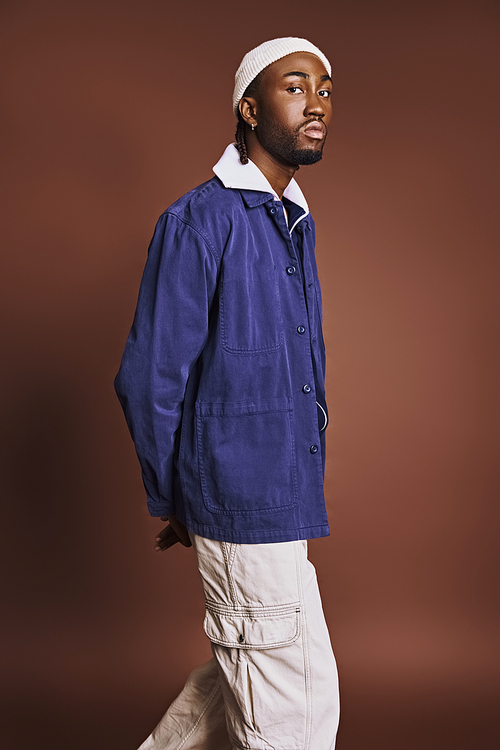 Handsome young African American man in blue jacket and white pants, confidently strolling.