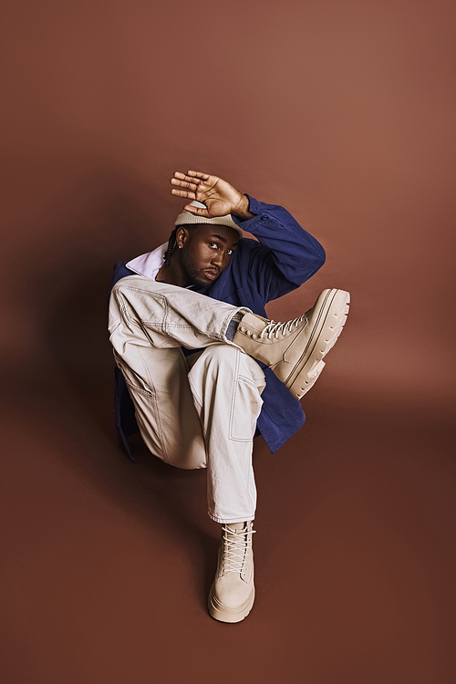 Handsome African American man in stylish outfit sitting on the ground with hands on head.