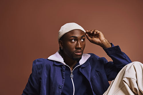 A young African American man exudes style in a blue jacket and white hat.