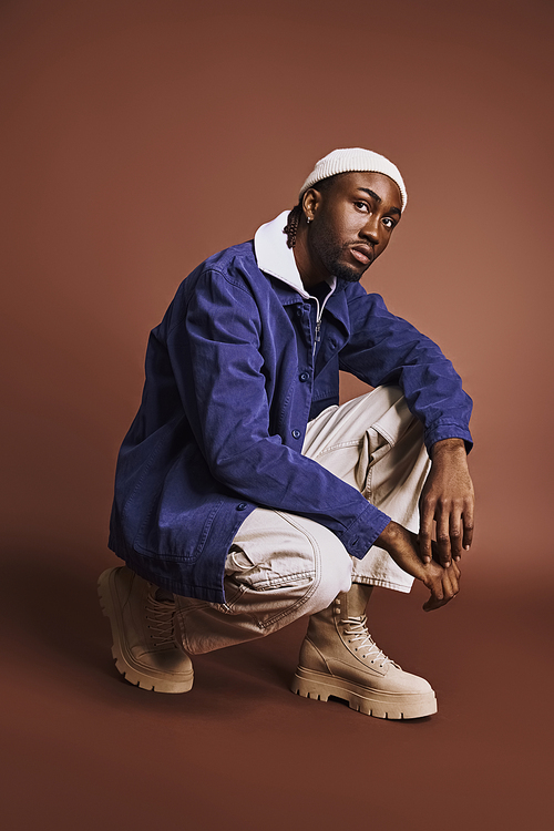 A handsome young African American man dressed in a stylish blue jacket and white pants.