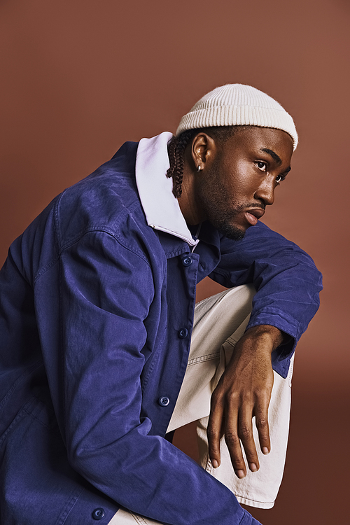 A handsome young African American man wearing a blue jacket and white hat.