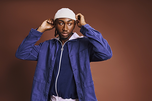 A handsome young African American man wearing a blue jacket and a white hat.