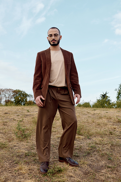 A handsome man poses confidently in a field, dressed in stylish autumn fashion amidst vibrant nature.