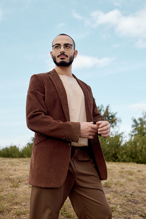 A handsome man dressed in stylish autumn clothing stands gracefully in a tranquil field.