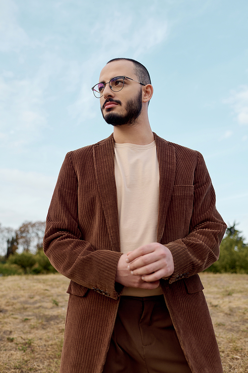 A fashionable man stands confidently in a field, embracing the vibrant autumn atmosphere with warmth.