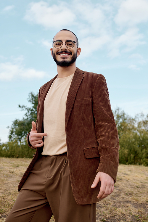 A well-dressed man showcases a warm autumn look while enjoying the tranquil beauty of nature.