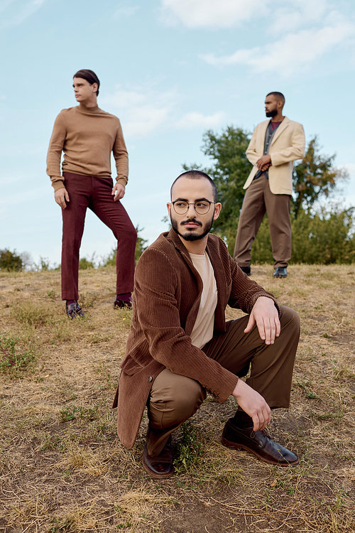 Three fashionable men showcase a trendy autumn wardrobe while enjoying the beauty of nature.