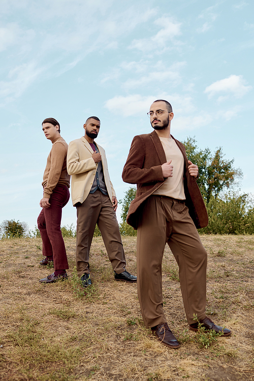 Three stylish men display their autumn fashion, standing confidently in a peaceful natural setting.