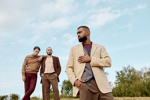 Three fashionable men confidently pose amidst golden autumn scenery, highlighting seasonal trends.