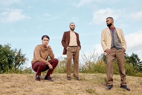 Handsome men dressed in autumn attire pose confidently in a peaceful field surrounded by nature.