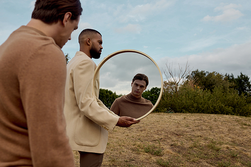 Two well-dressed men pose thoughtfully in an autumnal landscape, reflecting on their surroundings.