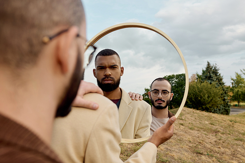 Two handsome men in chic autumn outfits are posing thoughtfully in a serene natural landscape.