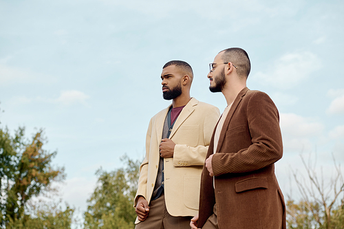 Two male models showcase trendy autumn outfits while standing confidently in a picturesque field.