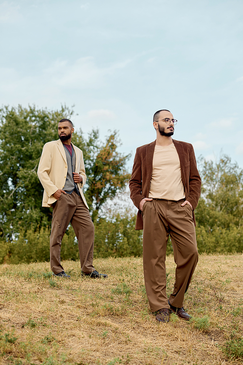 Two handsome men pose confidently in stylish autumn attire against a picturesque landscape backdrop.