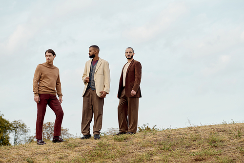 Three fashionable men pose together in a picturesque field, embracing the beauty of autumn charm.