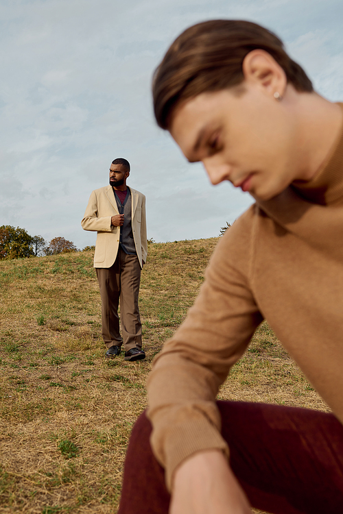 Two handsome men sport trendy autumn outfits while enjoying a peaceful moment in the fields.