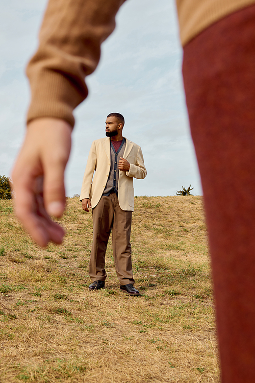 Handsome men dressed in elegant autumn attire pose confidently in a serene natural landscape.