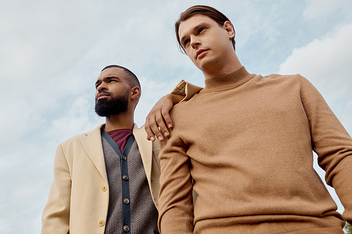 Two handsome men dressed in trendy autumn clothing pose elegantly in a beautiful field setting.