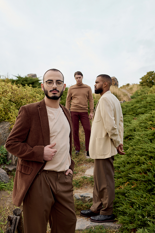 Three handsome men strike fashionable poses in a serene autumn field, showcasing stylish outfits.