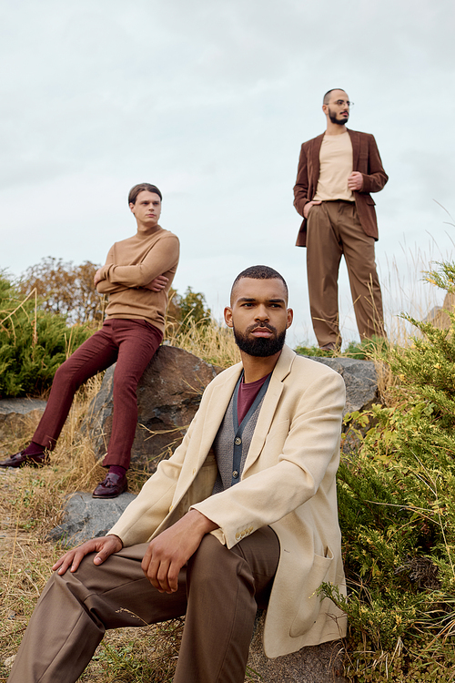 Three handsome men pose in a scenic field, embracing stylish autumn attire amid nature beauty.