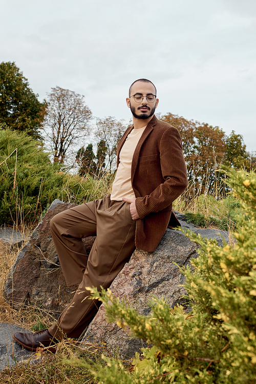 A handsome man showcases stylish autumn fashion while posing gracefully in a tranquil field of nature.