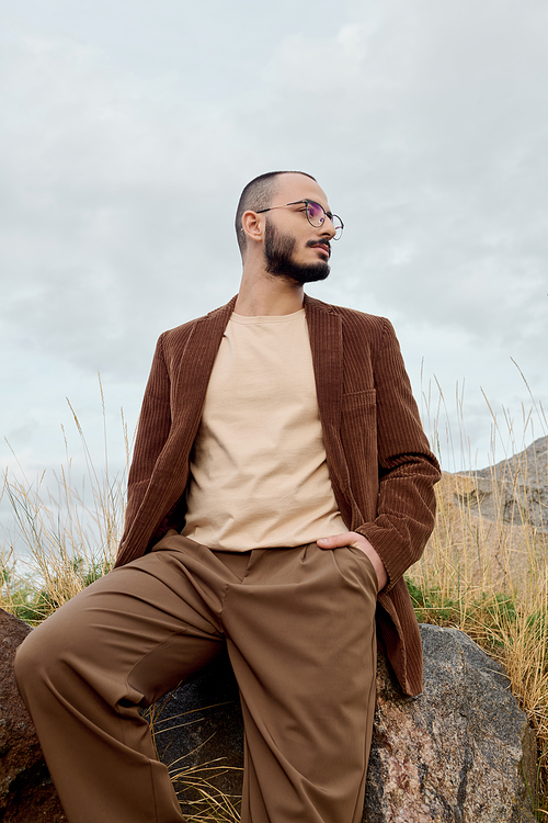 A man dressed in chic autumn attire stands confidently in a tranquil field, embracing the season beauty.