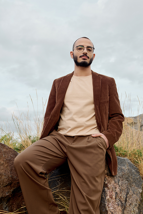 A handsome man poses confidently in stylish autumn attire against a scenic field backdrop.