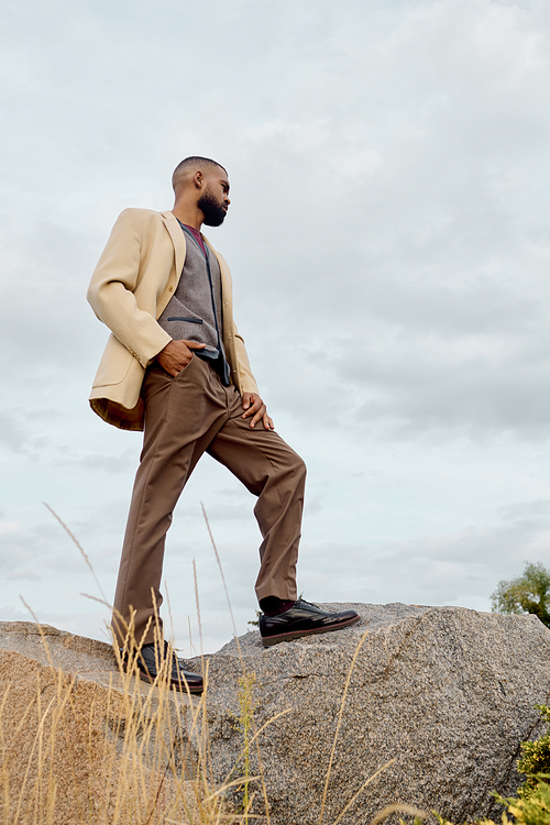 A dapper gentleman stands atop a rock, showcasing autumn fashion while surrounded by a tranquil field.