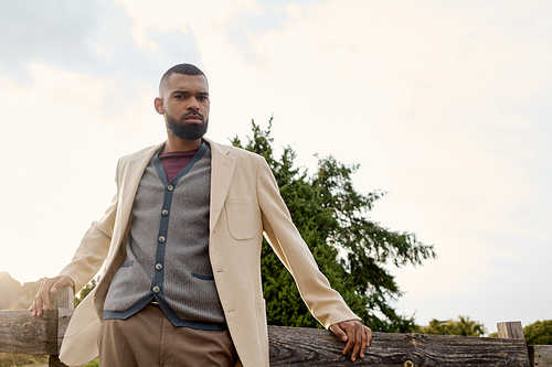 A handsome man stands confidently in a stunning autumn setting, showcasing his fashionable outfit.