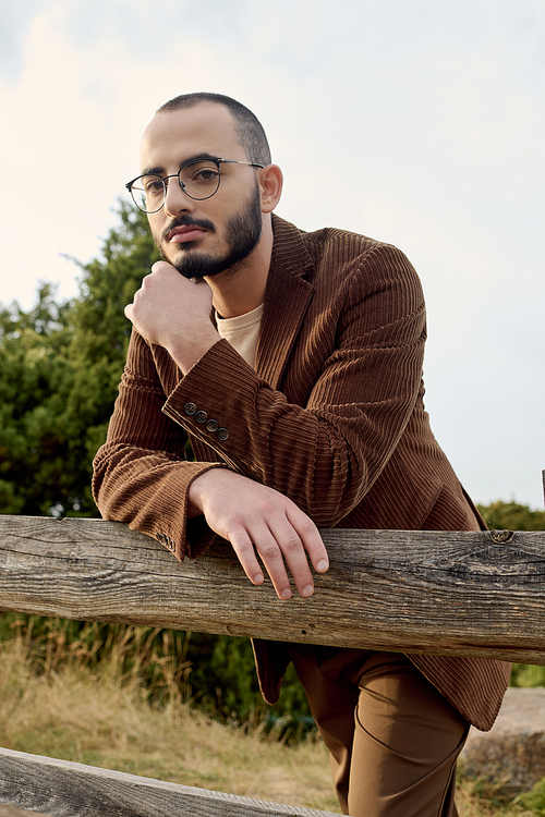 A handsome man dressed in autumn attire reflects the tranquil beauty of nature around him.