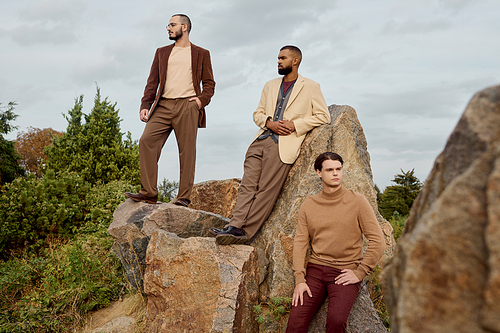 Three handsome men pose confidently in a picturesque field during the vibrant autumn season.