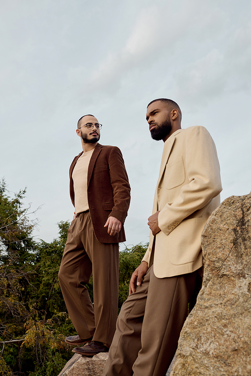 Handsome men pose in fashionable autumn attire, standing among lush greenery during a crisp fall day.