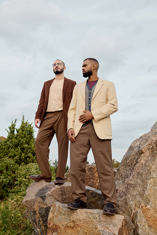 Two handsome men are posing in autumnal outfits, radiating style in a picturesque outdoor setting.