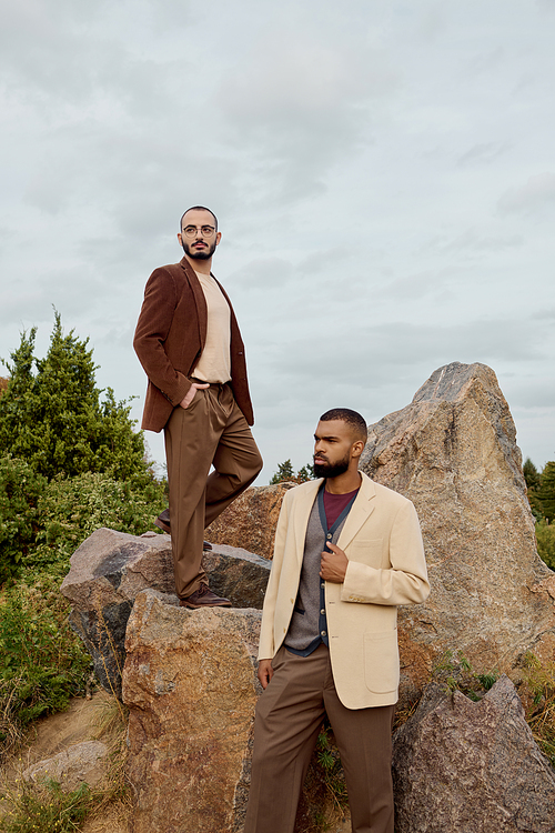 Two handsome men model chic autumn outfits while posing proudly in a picturesque outdoor setting.