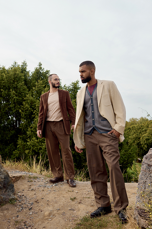 Two handsome men pose elegantly in autumn attire, surrounded by nature vibrant colors.