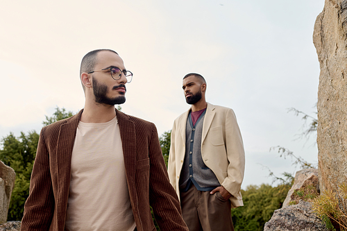 Two handsome men model autumn outfits surrounded by nature beautiful fall colors, exuding style and confidence.