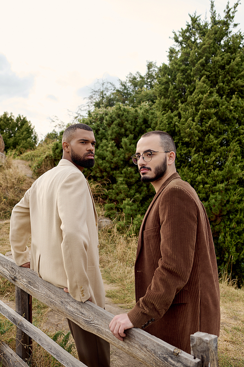 Two handsome men pose confidently in trendy fall attire amidst a serene autumn field setting.