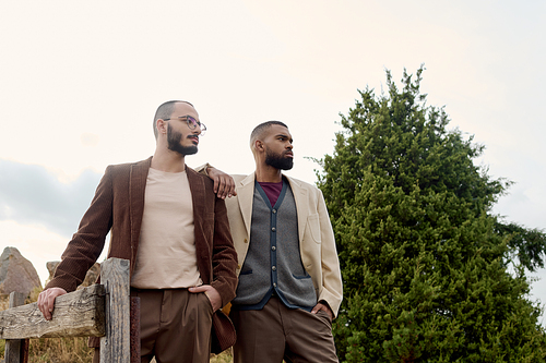 Two handsome men showcase their autumn fashion while standing in a tranquil field surrounded by nature.