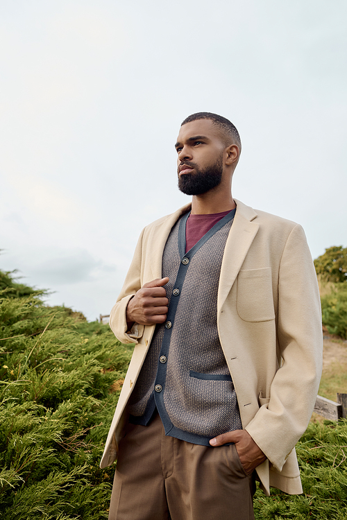 A handsome man stands confidently in a field, embracing autumn's beauty with his stylish attire.