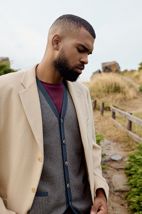 A handsome man in fashionable autumn attire gracefully poses amidst a tranquil field.