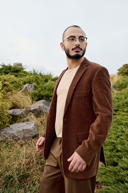 A well-dressed man stands confidently in a serene field, showcasing autumn fashion in a scenic setting.