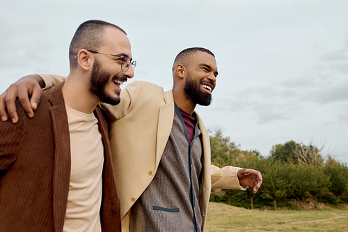 Two handsome men in fashionable outfits share a joyful moment while surrounded by autumn scenery.