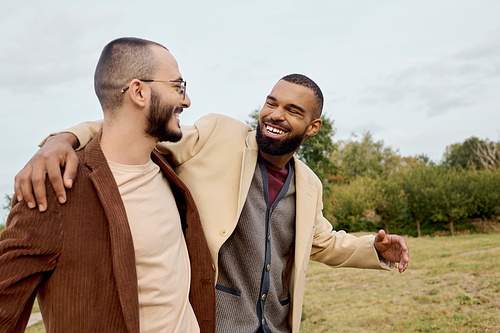 Two fashionable men share a joyful moment in a beautiful field, showcasing autumn style and friendship.